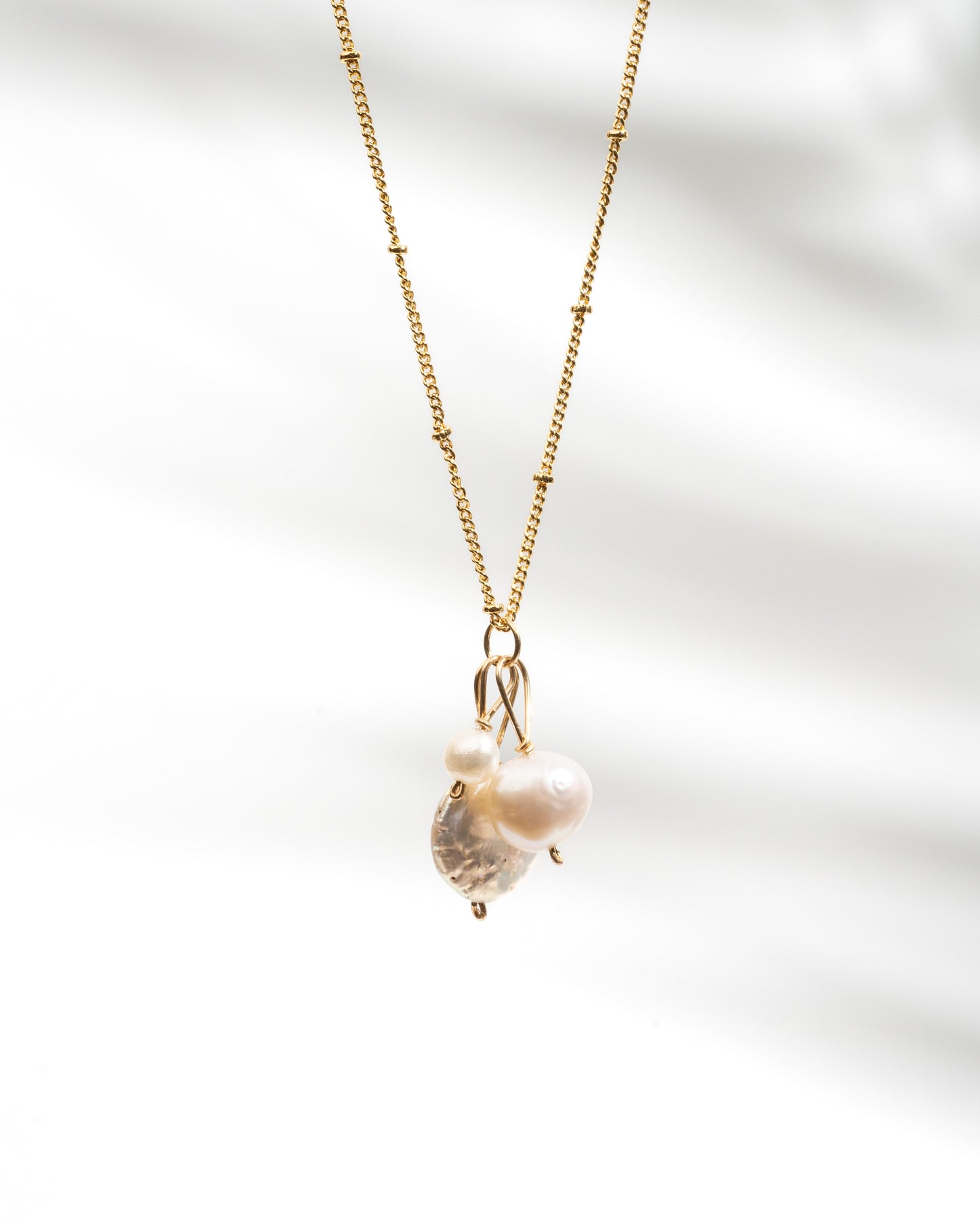 Close-up view of a trio pearl necklace featuring different-shaped and sized genuine pearls suspended on a delicate 14K gold fill chain. The pearls exhibit a lustrous finish, while the necklace showcases a waterproof and tarnish-proof design for worry-free wear. A timeless and elegant accessory that adds sophistication to any outfit."